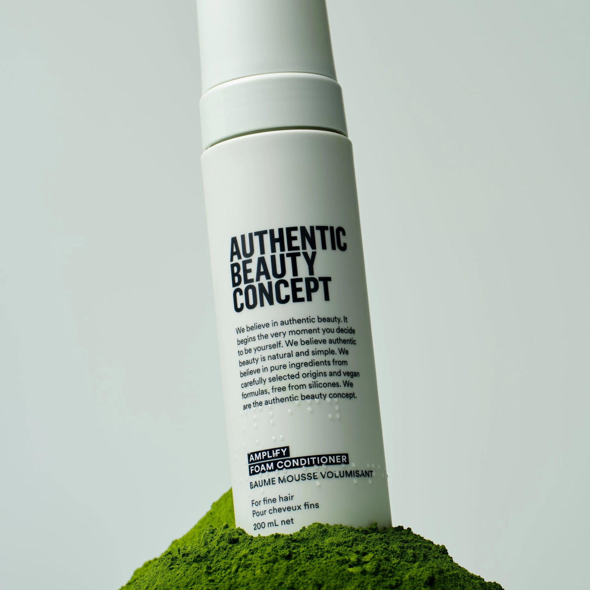 White bottle of 'Authentic Beauty Concept' conditioner on a green mound with a gray background
