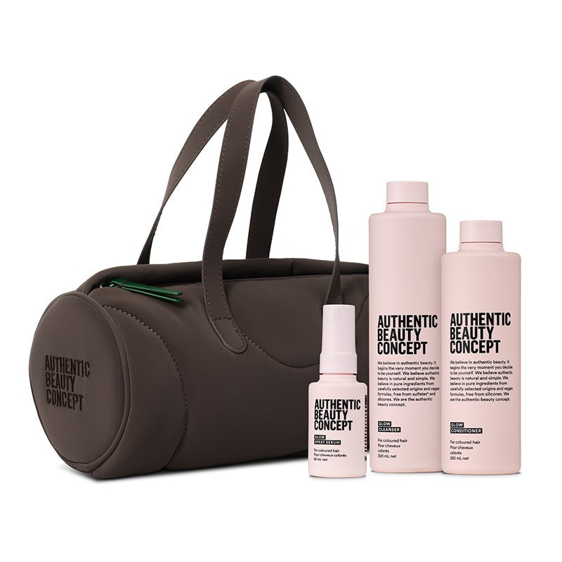 A dark brown barrel cosmetic bag with dual handles, shown alongside three matching pink skincare bottles labeled 'AUTHENTIC BEAUTY CONCEPT' on a clean white background.